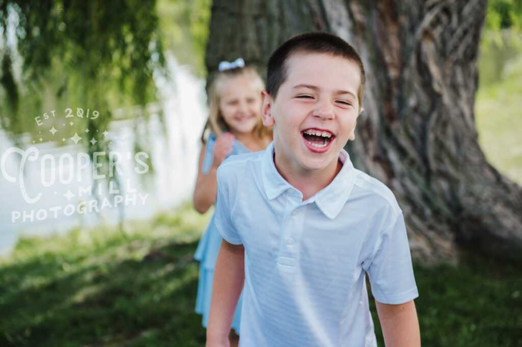 Boy laughs in front of sister by willow tree