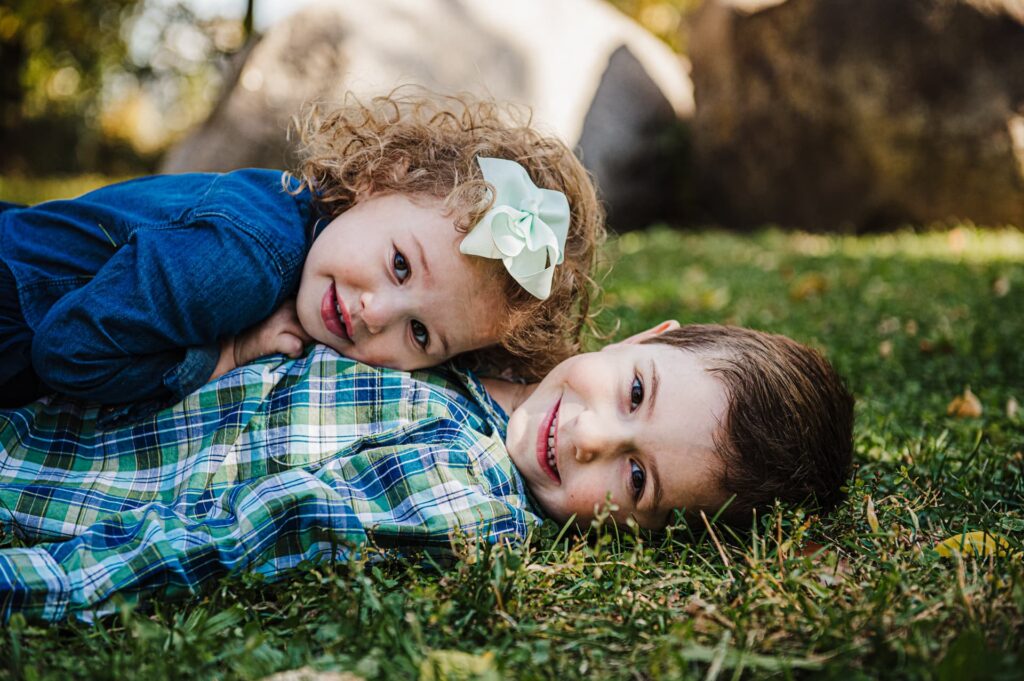 a sister lays on top of her brother in the grass