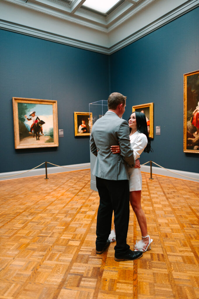 Bride and groom embrace inside a gallery at the Art Institute of Chicago, surrounded by classical paintings on deep blue walls, after their downtown elopement